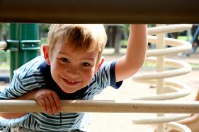 Image of boy smiling in playground with trees in background near Myers Park Dental Partners.