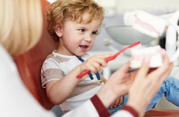 Little boy sitting in dental exam chair and holding tooth brush