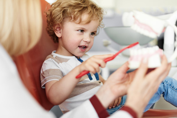 Little boy brushing teeth on dental model while sitting in dental chair