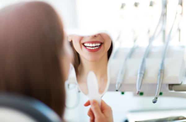 Woman looking at her smile in a mirror after getting restorative dental treatment at Myers Park Dental Partners in Charlotte, NC